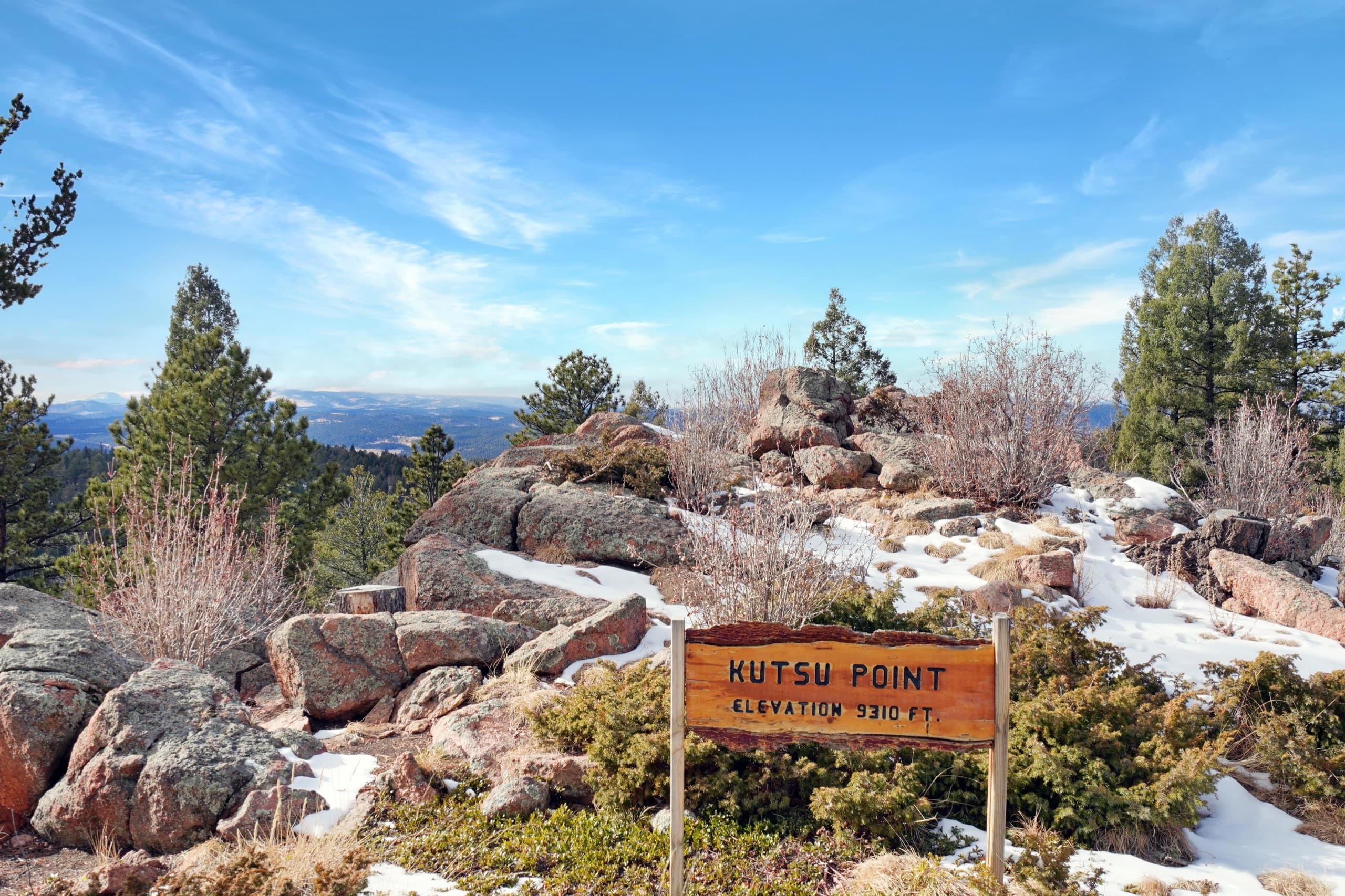 The carved Kutsu Point summit marker at 9,310 feet, on the property's rocky high point above a wide Rocky Mountain view