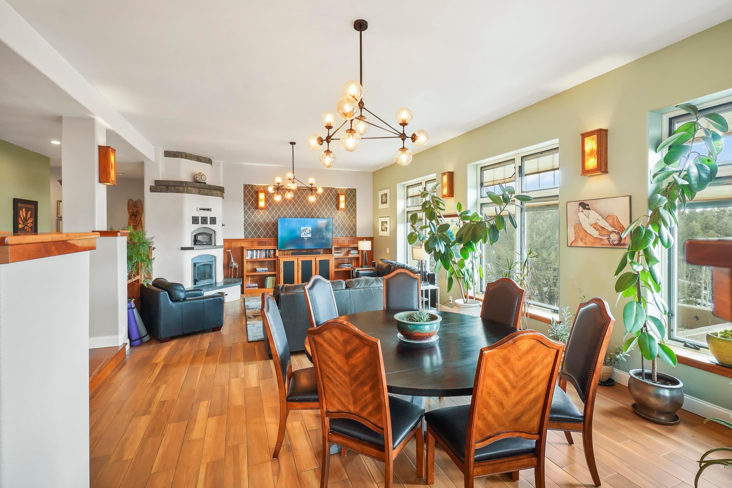 The great room at Kutsu Point: a round dining table, a kiva fireplace, and walls of windows onto the pines